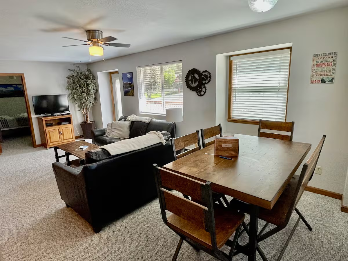 Open living and dining area with a dining table, a television on a stand and windows on two sides