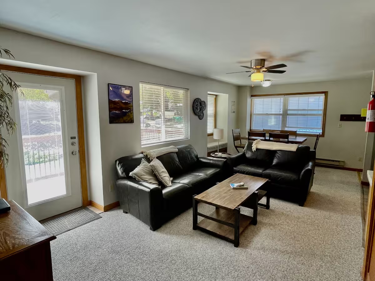 Living room with a black leather sofa and loveseat, a coffee table and a door out to the deck