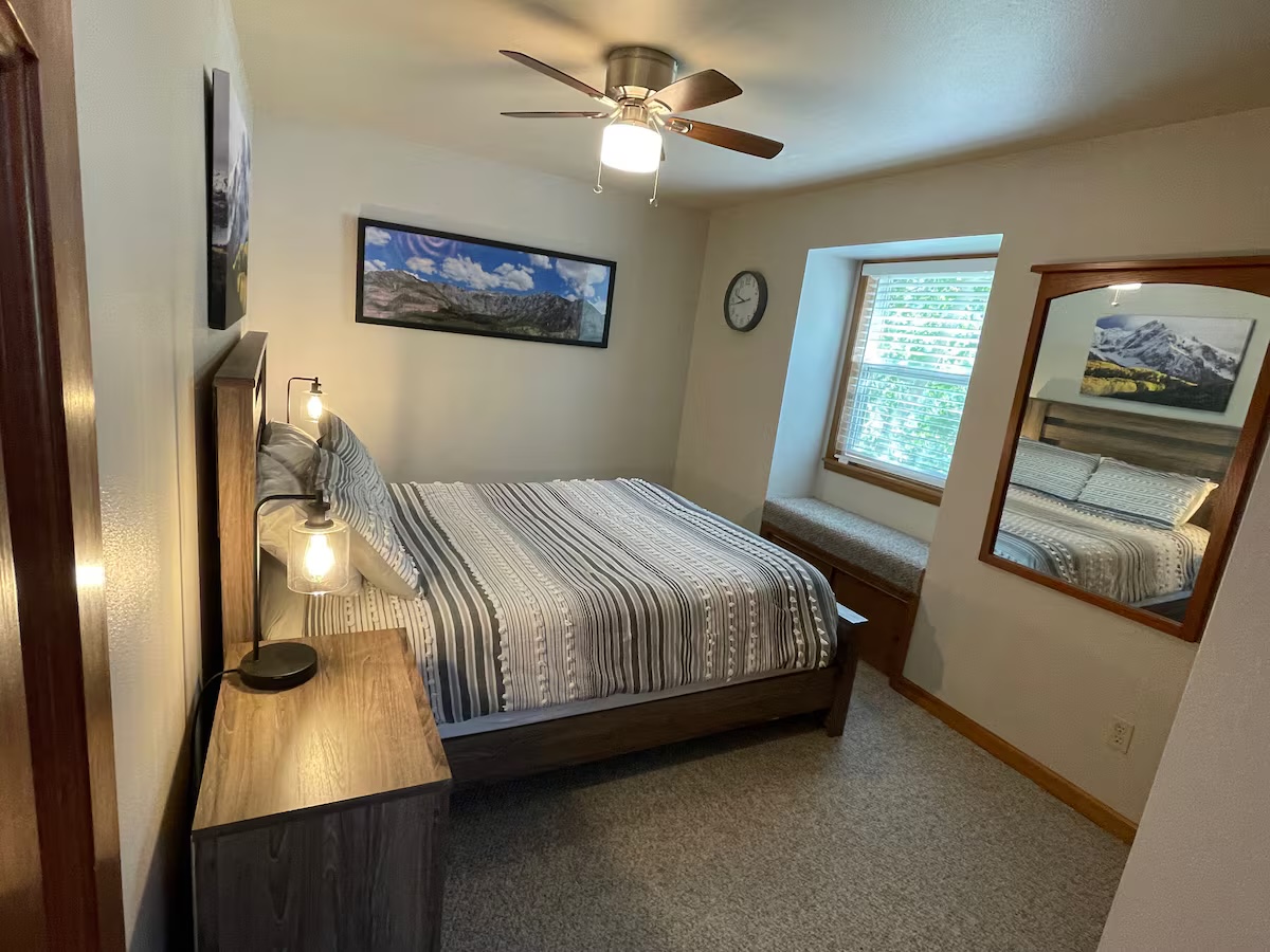 Bedroom with a wood headboard, bedside lamps, a window seat and a framed mountain panorama above the bed