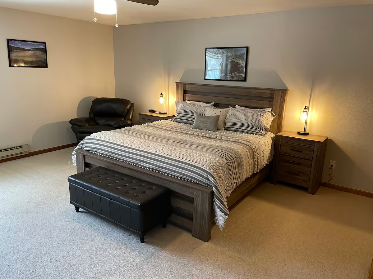 Bedroom with a wood headboard, bedside lamps, a recliner and a storage bench at the foot of the bed