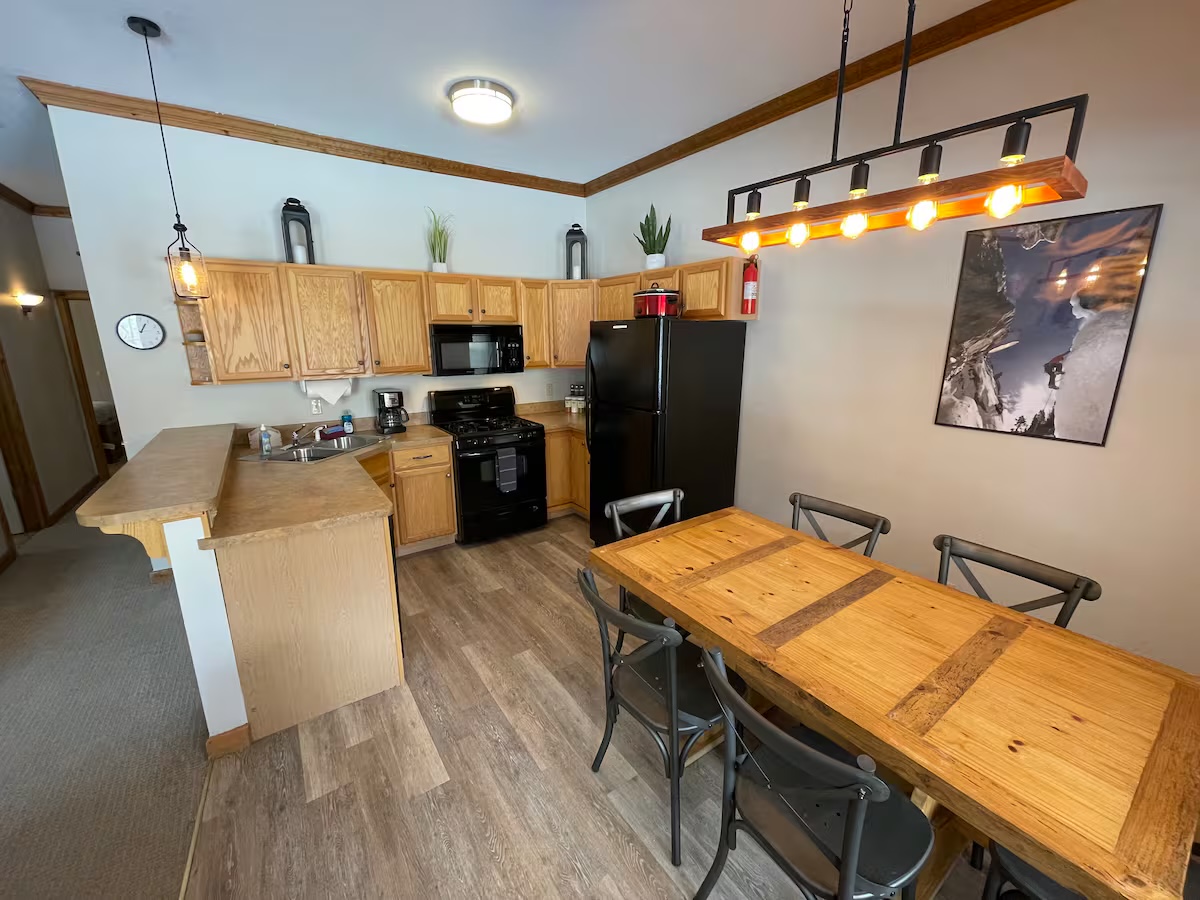 Kitchen with oak cabinets, a black refrigerator and gas range and a breakfast bar, with the dining table beneath a framed ice-climbing photograph