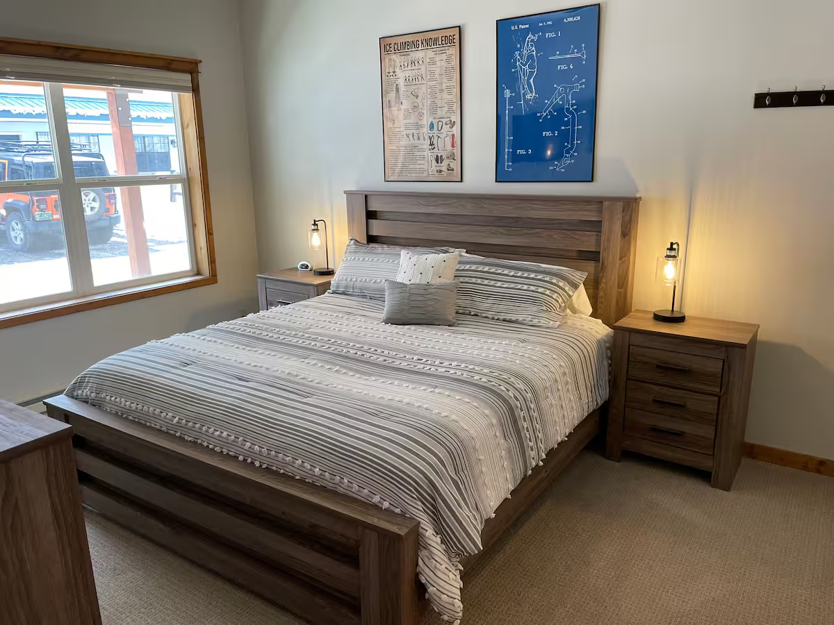 Bedroom with a wood headboard, bedside lamps and an ice-climbing chart and patent print above the bed