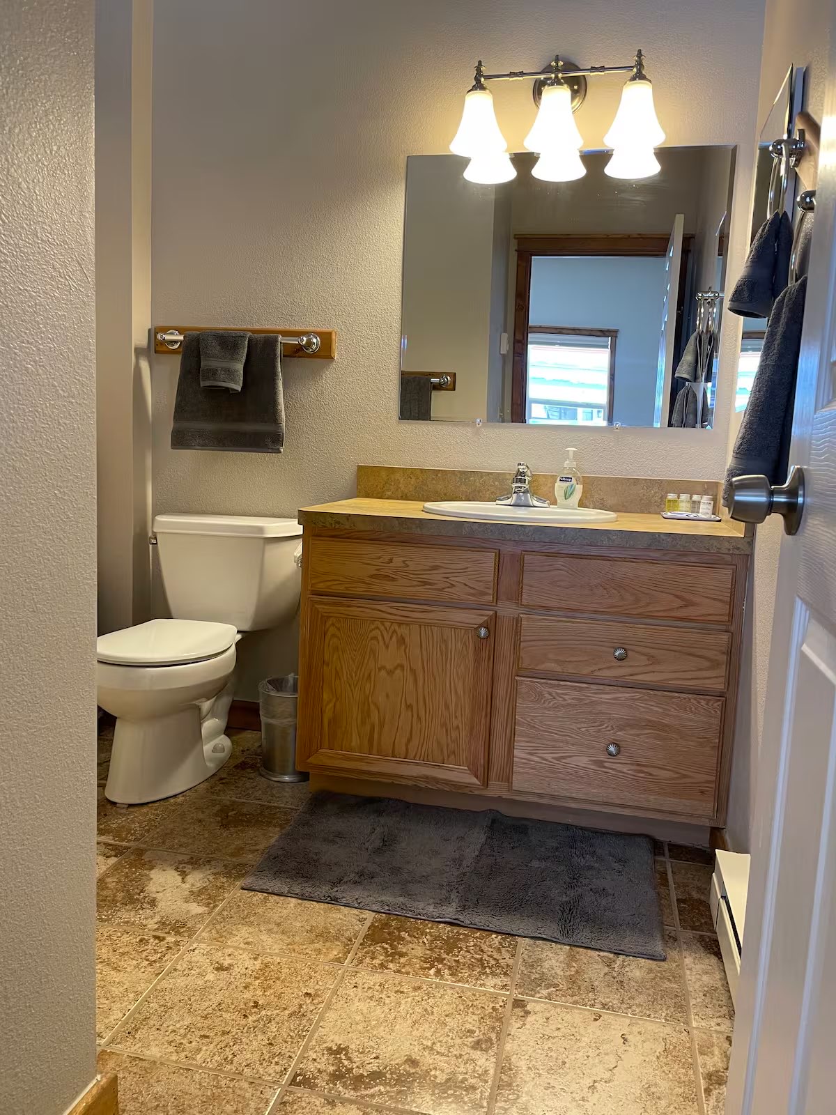 Bathroom with an oak vanity, a wide wall mirror and a tiled floor